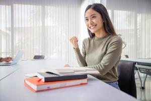 asiatiska kvinnliga studenter ler och upprymd med armarna höjda. Hon läser boken och recenserar även boken innan provet foto