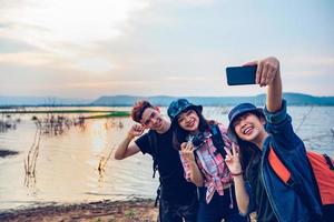 asiatisk grupp ungdomar med vänner och ryggsäckar som går tillsammans och glada vänner tar foto och selfie, koppla av på semesterkonceptresor