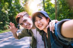 asiatisk grupp ungdomar med vänner och ryggsäckar som går tillsammans och glada vänner tar foto och selfie, koppla av på semesterkonceptresor