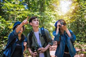 asiatisk grupp ungdomar som vandrar med vänner ryggsäckar går tillsammans och tittar på karta och tar fotokamera vid vägen och ser lyckliga ut, slappna av på semester konceptresor foto