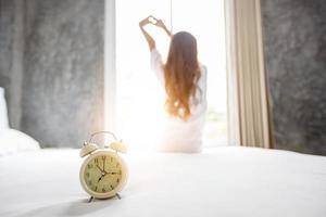 asiatisk kvinna vaknar upp i sin säng helt utvilad och öppnar gardinerna på morgonen för att få frisk luft. foto