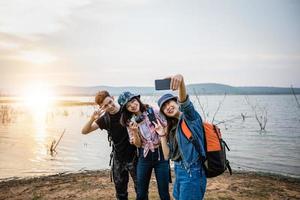 asiatisk grupp ungdomar med vänner och ryggsäckar som går tillsammans och glada vänner tar foto och selfie, koppla av på semesterkonceptresor