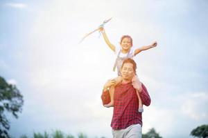 asiatisk flicka och pappa med en drake springande och glad på ängen på sommaren i naturen foto