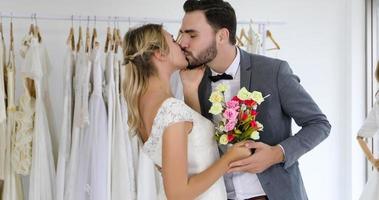 älskare ger blommor till bruden och kysste glada och par älskar stående i bröllop studio foto