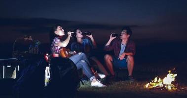 en grupp asiatiska vänner turist dricker och spelar gitarr tillsammans med lycka på sommaren medan de campar nära sjön i solnedgången foto