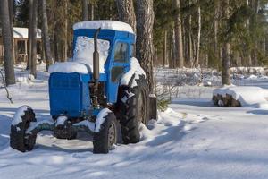 snötäckt traktor i skogen nära byn. foto