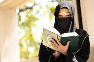 muslim niqaab kvinna läsa och inlärning de quran och tro de helig al quran bok. arab saudi svart chador lady. foto