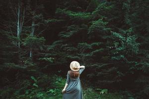 kvinna i en stråhatt och klänning står på en bakgrund av grön skog och träd foto