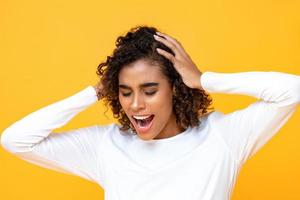 närbild porträtt av förvirrad afrikansk amerikansk kvinna som skriker medan hon håller hennes huvud med båda händerna i isolerad studio gul bakgrund foto
