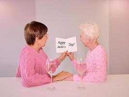 två mogna kvinnor som dricker vin och ger ett vykort. vänskap, semester, kärlek, samkönade äktenskap koncept foto