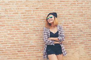 ung söt hipster kvinna står mot tegelvägg poserar leende njuta med trevlig tid. foto