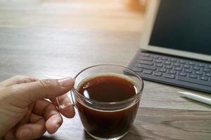hand som håller kaffekopp eller te och digital bordsdocka smart tangentbord, penna på träbord, filtereffekt foto