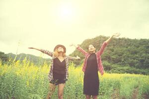 två hipster kvinna reser och höjer händerna njuter med blomma fält tillsammans, avkopplande god tid solig dag. foto