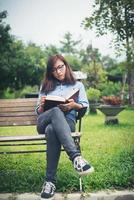 hipster charmig tjej koppla av i parken medan du läser bok, njut av naturen runt. foto