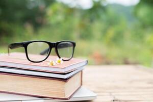 bok och glasögon för att läsa och skriva över suddig natur utomhus bakgrund. foto
