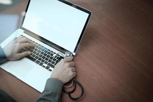 ovanifrån av medicin läkare hand som arbetar med modern dator och smart telefon på trä skrivbord som medicinskt koncept foto