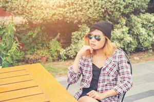 utomhus porträtt av ung hipster kvinna sitter ensam på gamla staden café och väntar på sin pojkvän bär rutig outfit och solglasögon. foto