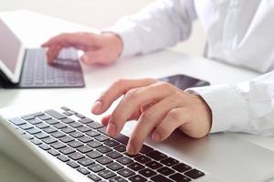 närbild av affärsman som skriver digital surfplatta med tangentbord och bärbar dator på vitt skrivbord i moderna kontor foto