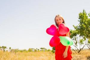 en tonårsflicka med ballonger i en röd sommarklänning mot bakgrund av naturen en solig dag. foto