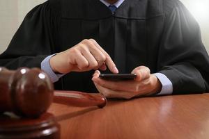 rättvisa och lag koncept. manlig domare i en rättssal med klubban, arbetar med smart telefondator på träbord foto