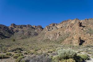 berg och buskar nära vulkanen teide, delvis täckt av moln. klarblå himmel. teide nationalpark, teneriffa, kanarieöarna, spanien. höjd 2100 meter. foto