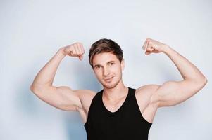 muskulös ung man visar biceps i svart t-shirt på en vit bakgrund. kopiera, tomt utrymme för text foto