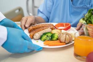 asiatisk senior eller äldre gammal dam kvinna patienten äter frukost och grönsaker hälsosam mat med hopp och glad medan du sitter och hungrig på sängen på sjukhuset. foto