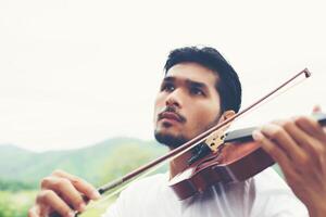 ung hipster musiker man spelar fiol i naturen utomhus livsstil bakom berget. foto