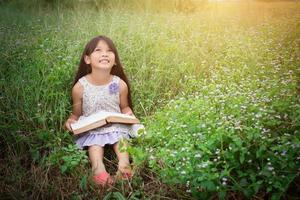 liten söt asiatisk flicka som läser bok i naturen. foto
