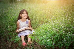 liten söt asiatisk flicka som läser bok i naturen. foto