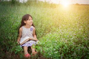 liten söt asiatisk flicka som läser bok i naturen. foto