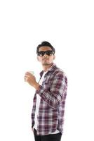 porträtt av stilig ung hipster man står, bär solglasögon, skjorta och håller en kopp kaffe på isolerad vit bakgrund. foto