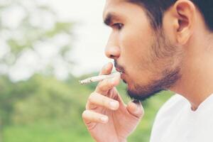 ung hipster man tar vila, röker cigarett med naturen och frisk bris. foto