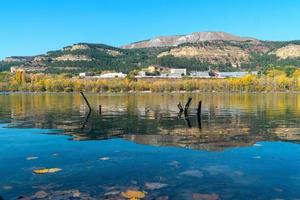 gula lönnlöv på den blå ytan av sjön. reflektion av hösten skog och berg bakgrund foto