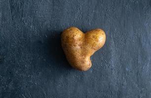 potatis i form av ett hjärta på mörk bakgrund. grönsak av ovanlig form foto