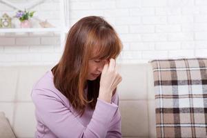 brunett medelålders kvinna med huvudvärk på hem bakgrund. klimakteriet foto