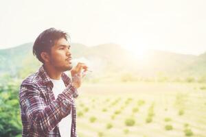 hipster man röker cigarett, står bakom ett berg. bland den friska luften på morgonen. foto