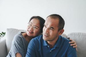 porträtt av asiatiska mogna par som sitter i vardagsrummet. fru och man kramas, håller handen med lycka och glada. kärlek, säkerhet och försäkring familj koncept foto