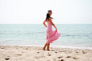 vacker kvinna med lång rosa klänning på en tropisk strand foto