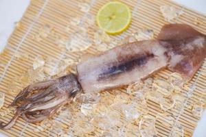 färska bläckfiskar bläckfisk eller bläckfisk för lagad mat på restaurang eller skaldjursmarknad, rå bläckfisk på is med salladskryddor citronlime på träbakgrunden foto