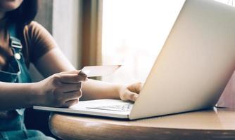 närbild kvinna hand som håller kreditkort och skriva tangentbord laptop om shopping online koncept. foto