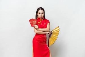 asiatisk kvinna i orientalisk cheongsam-dräkt som håller röda kuvert ang pow och fläkt poserar på ljusgrå studiobakgrund för kinesiska nyårskoncept, utländska texter betyder stor lycka stor vinst foto