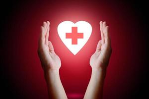 sjukvård koncept, kvinna hand som håller och skydda hjärtat med medicinsk symbol inuti på röd bakgrund. foto