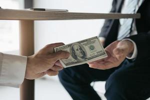 entreprenörer får pengar under skrivbordet som är en muta av deras partners som båda är korrupta i företagsrummet. foto