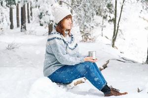 kvinna med en kopp te i händerna i en snötäckt skog foto