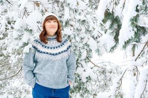 vacker kvinna i en varm hatt och tröja på en bakgrund av snöig skog foto