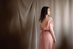 vacker brunett kvinna i en rosa klänning på en bakgrund av linnetyg. kopiera, tomt utrymme för text foto