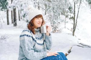 vinter kvinna porträtt med en kopp te i händerna i en snötäckt skog. kopiera, tomt utrymme för text foto