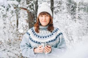porträtt av en kvinna med en kopp te i händerna på en bakgrund av snöig skog foto