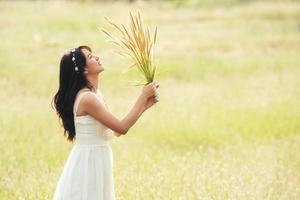 ung glad kvinna vit klänning med armarna fånga en gräsmatta i grönt guld foto